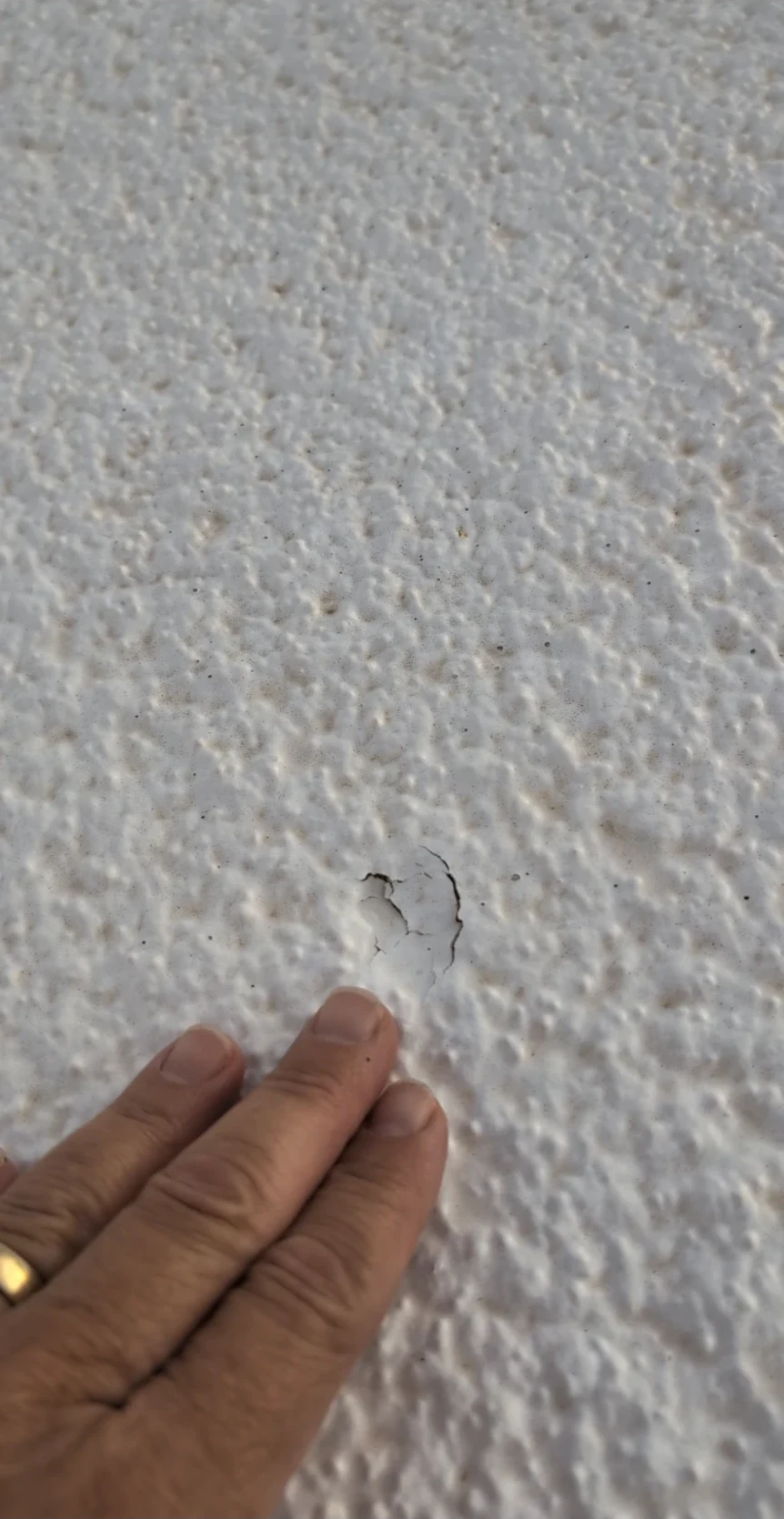 A hand points to cracked coating at a hail impact on a foam roof